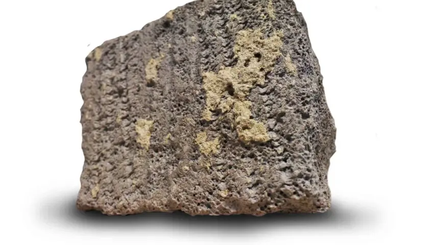 Ett stycke porös sten med mörkgrå och gulaktiga partier. Dess blåbetong utseende ger en känsla av naturlig textur.