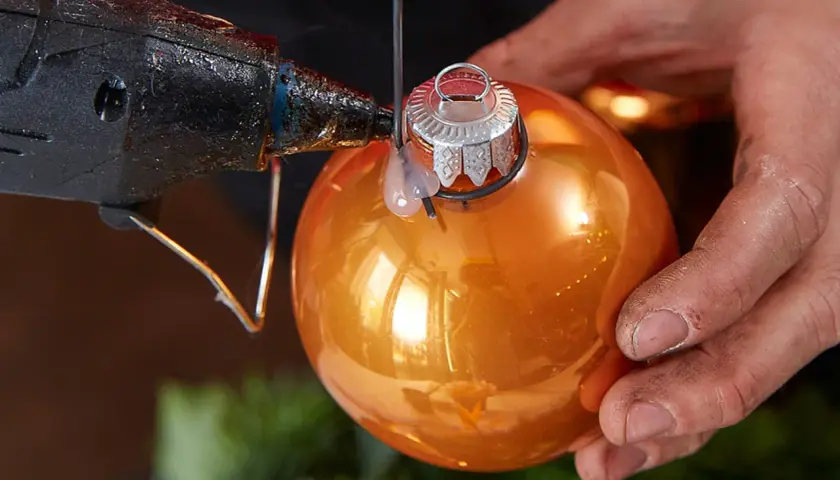 Mit Klebepistole und orangefarbener Kugel einen Adventskranz aus Kugeln selber basteln.