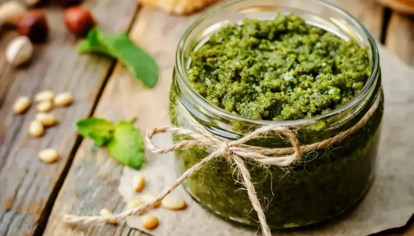 Słoik domowego pesto, ozdobiony sznurkiem, z orzeszkami pinii i listkami bazylii. Idealny przepis, jak zrobić pesto.