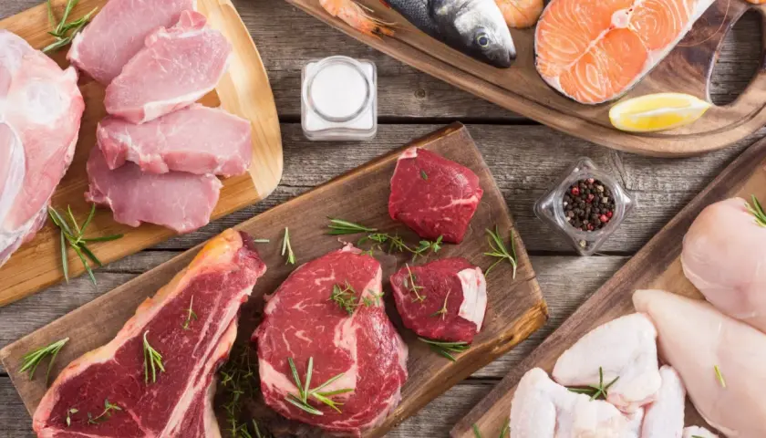 Mięso i ryby na deskach, jak na diecie karniwora. Co to? Surowe steki, schab, łosoś, kurczak, krewetki, ryba morska.