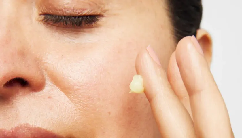 Närbild på en persons ansikte med slutna ögon. Ett finger med en klick kräm, kanske för att visa retinol resultat.