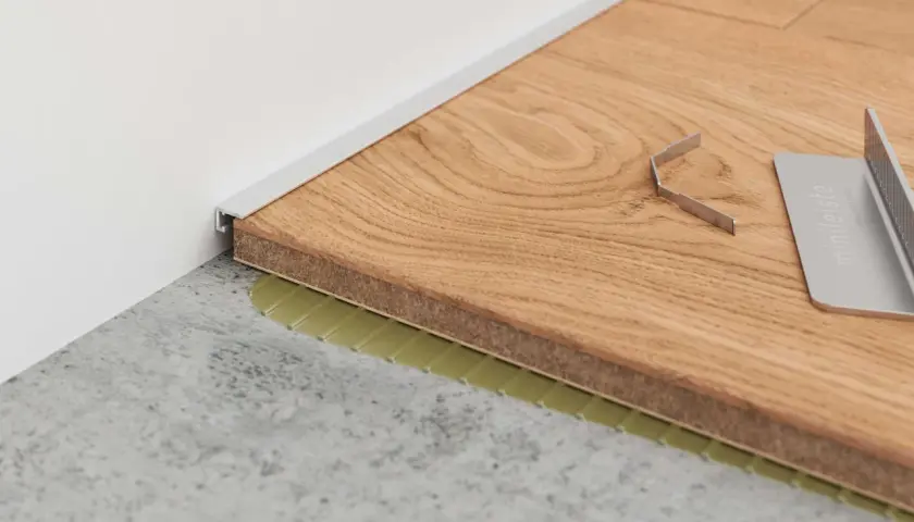 Moderne Alternative zu Sockelleisten: Ein schmales Metallprofil schließt den Boden zur Wand ab. Werkzeug liegt bereit.