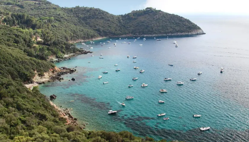 Baie pittoresque de Tirrenia, Italie, avec de nombreux bateaux naviguant sur des eaux turquoise cristallines bordées de collines verdoyantes.