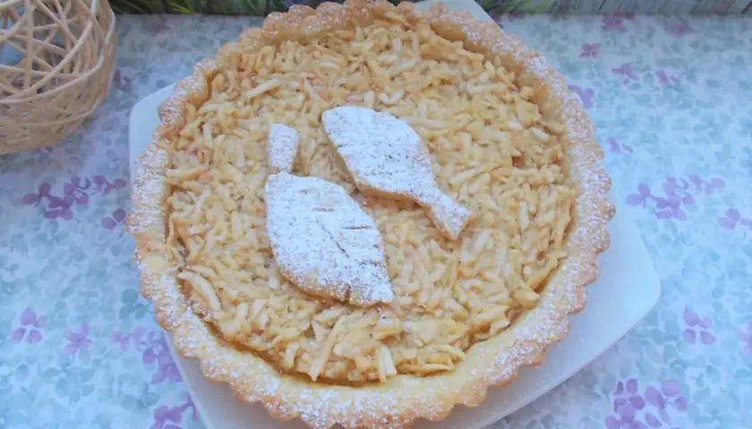 Pyszna tarta z jabłkami, posypana cukrem pudrem, z dwoma listkami z ciasta na wierzchu. Idealna na deser.