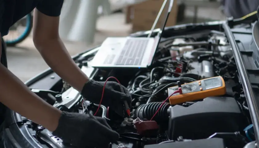 Mechanik diagnozuje objawy pompy wysokiego ciśnienia 1.6 THP za pomocą multimetru i laptopa przy otwartej masce samochodu.