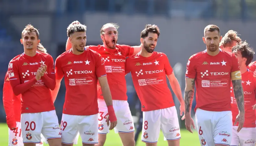 Piłkarze Wisły Kraków w czerwonych strojach, dyskutują o potencjalnych transferach.
