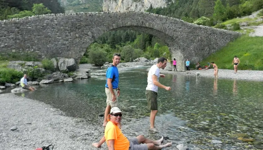 Gente disfrutando del río bajo el puente de piedra en Bujaruelo, con vistas al Taillón.