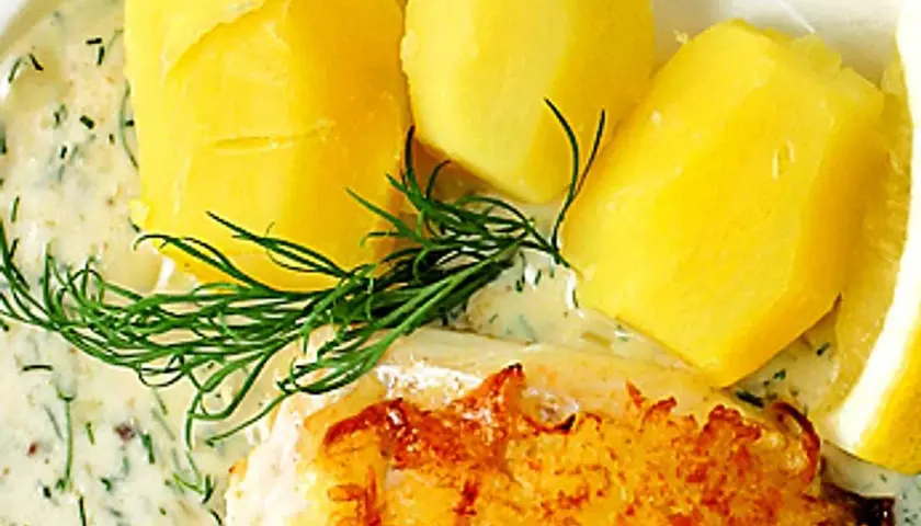 En gyllene fiskbit med krämig dillsås till fisk, serverad med kokt potatis och en citronskiva.