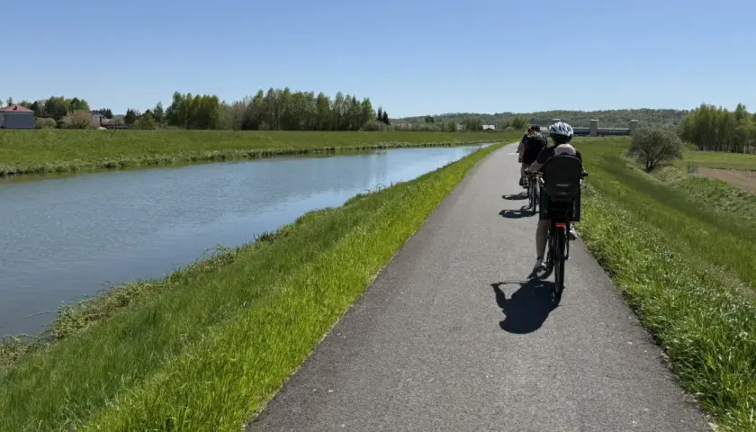 Rodzina na rowerach wzdłuż kanału. Słoneczny dzień sprzyja rodzinnemu **velo skawa** pośród zielonych łąk i drzew.