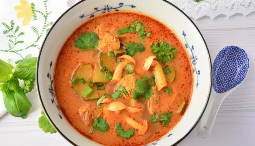 Aromaticzna zupa tom yum z kurczakiem, grzybami i kolendrą w misce z niebieskim wzorem. Obok leży łyżka.