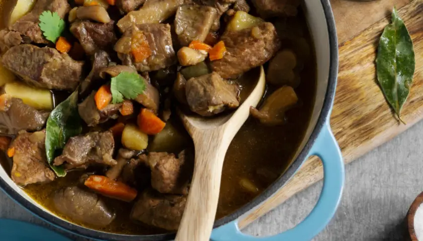 Un savoureux navarin d'agneau, aux carottes et pommes de terre, mijote dans une cocotte bleue. Son origine est un délice.