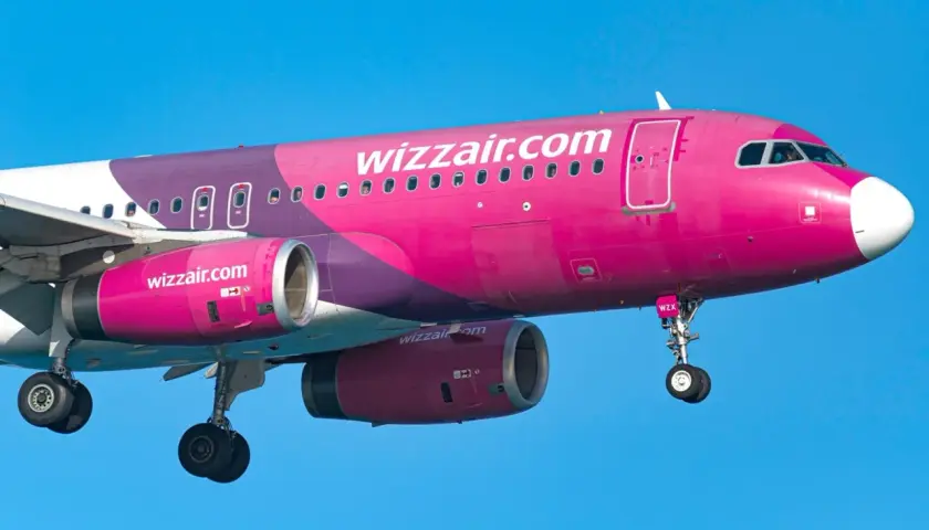 Różowy samolot Wizzair z fioletowymi elementami na tle błękitnego nieba.