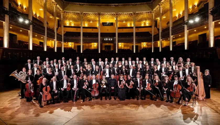 Kungliga Filharmonikerna medlemmar poserar i en stor orkestersal.