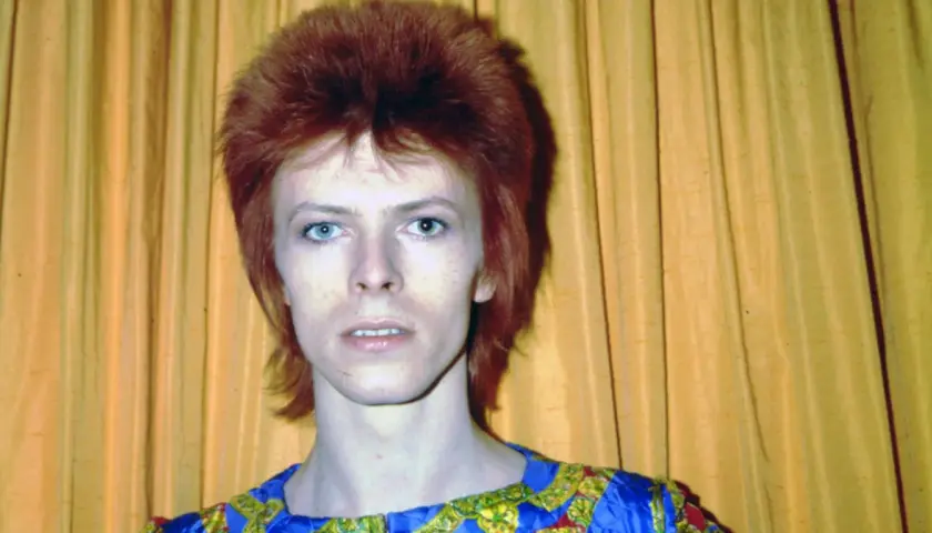 Ikoniczny David Bowie z burzą rudych włosów i niebieskimi oczami, w stroju przypominającym jego słynne kreacje. Jego muzyka, jak te utwory, wciąż inspiruje.