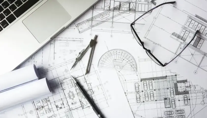 Na stole leżą plany architektoniczne, laptop, cyrkiel, linijka i okulary. To idealne miejsce do pracy nad kosztorysem budowlanym wzór.