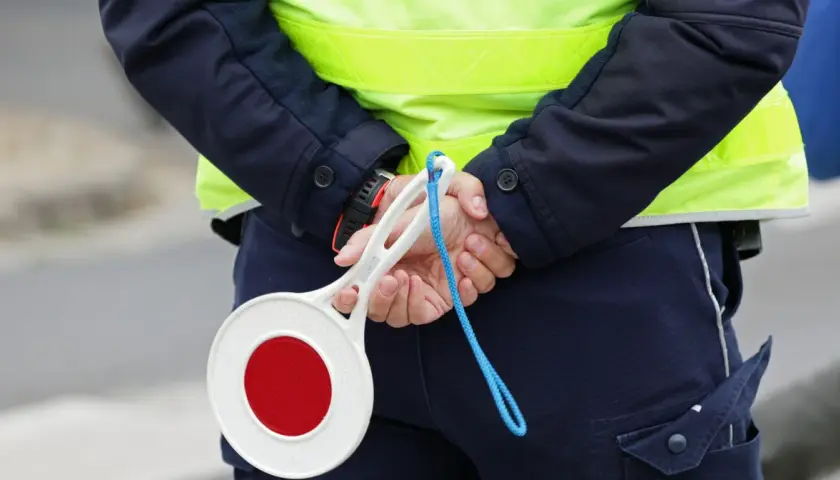Policjant w kamizelce odblaskowej trzyma znak stop. Zastanawiasz się, ile km można jechać na autostradzie?