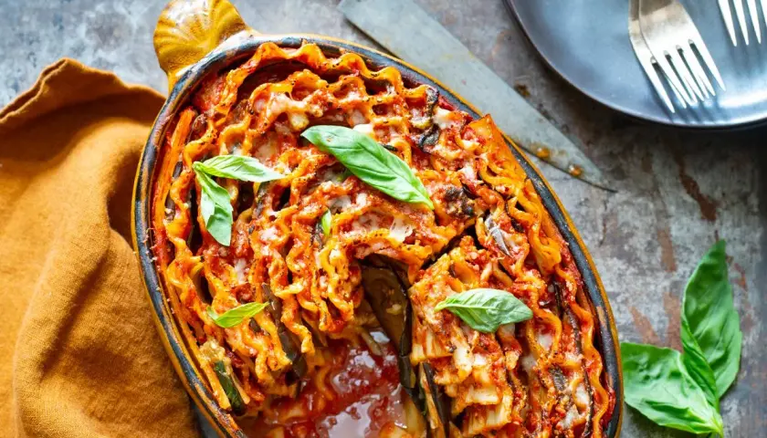 Lasagne aubergine italienne gratinée, garnie de feuilles de basilic frais, dans un plat ovale en terre cuite.