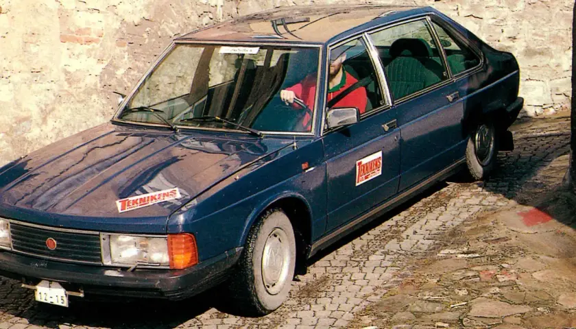 Mörkblå tatra bil med "Teknikens Värld"-logga på huven och dörren. En man i röd tröja kör.