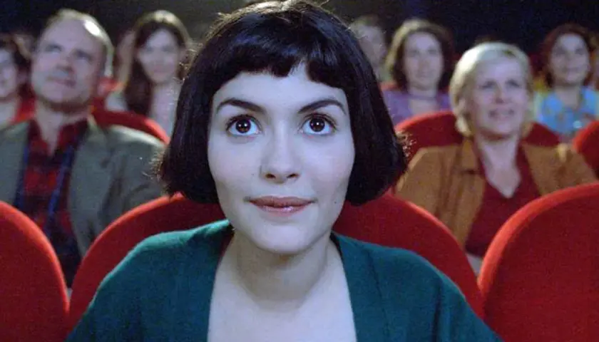 Amelia z uśmiechem na twarzy ogląda filmy podnoszące na duchu w kinie, otoczona innymi widzami.