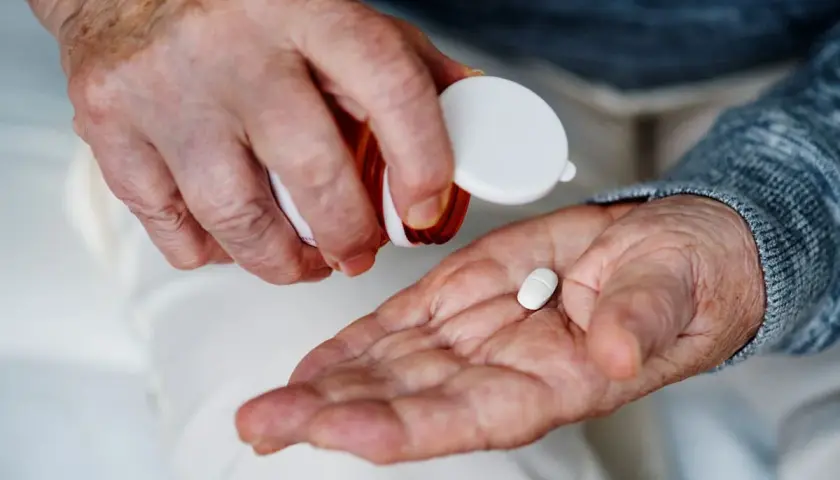 Manos de anciano vertiendo una pastilla blanca en su palma para tomar magnesio.