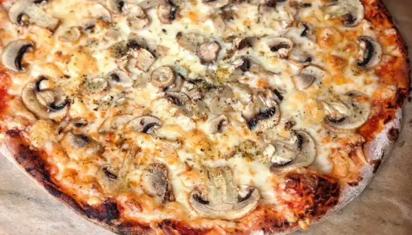 Pyszna pizza capricciosa z pieczarkami i ciągnącym się serem, idealna na wieczór z przyjaciółmi.