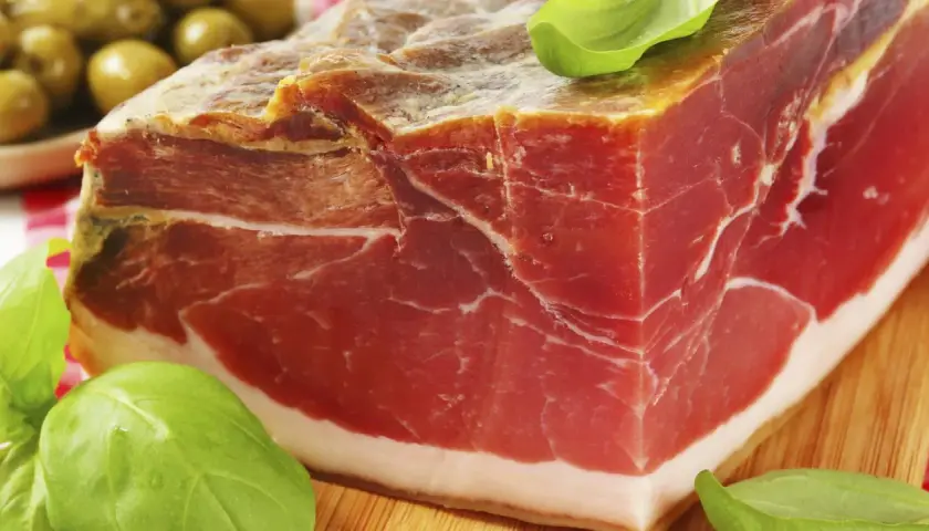 Ein Block Parma-Schinken, mariniert mit Kräutern, daneben grüne Oliven. Was ist Parmaschinken? Ein Genuss!