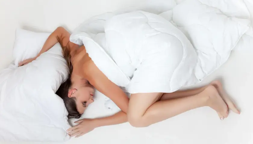 En andfådd gravid kvinna sover på sidan, insvept i ett vitt täcke.