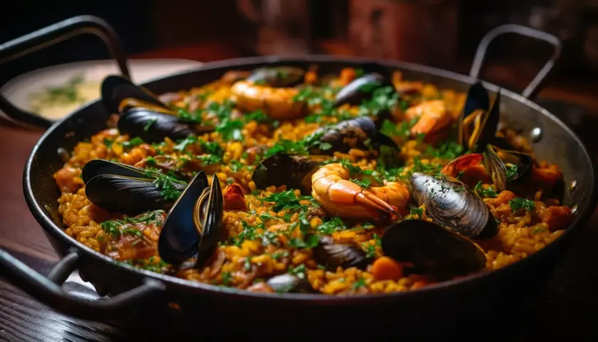 Un plat de paella aux fruits de mer, garni de moules et de crevettes, prêt à être dégusté avec un verre de vin rouge.