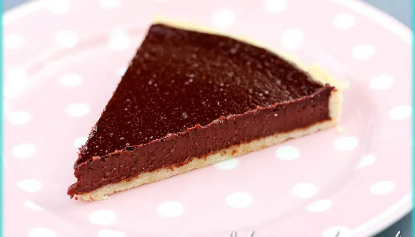Une part de tarte au chocolat facile, avec une garniture riche et une pâte croustillante, servie sur une assiette rose à pois blancs.