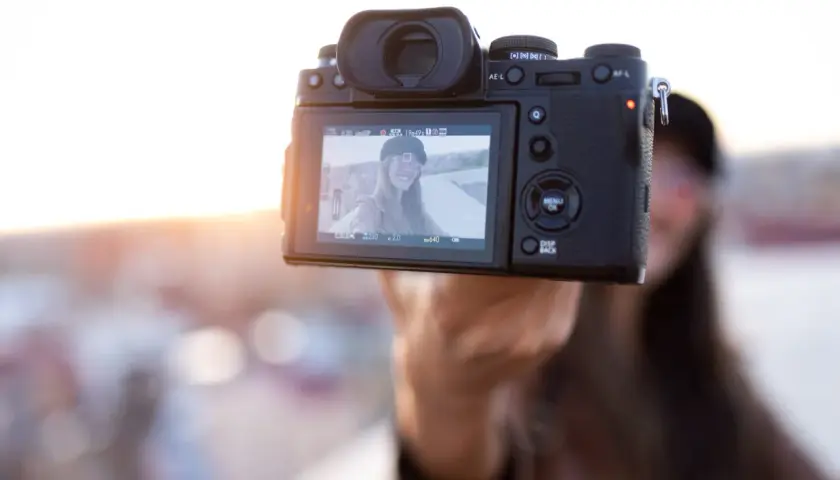 Aparat fotograficzny trzymany przez rękę, na ekranie selfie uśmiechniętej kobiety.