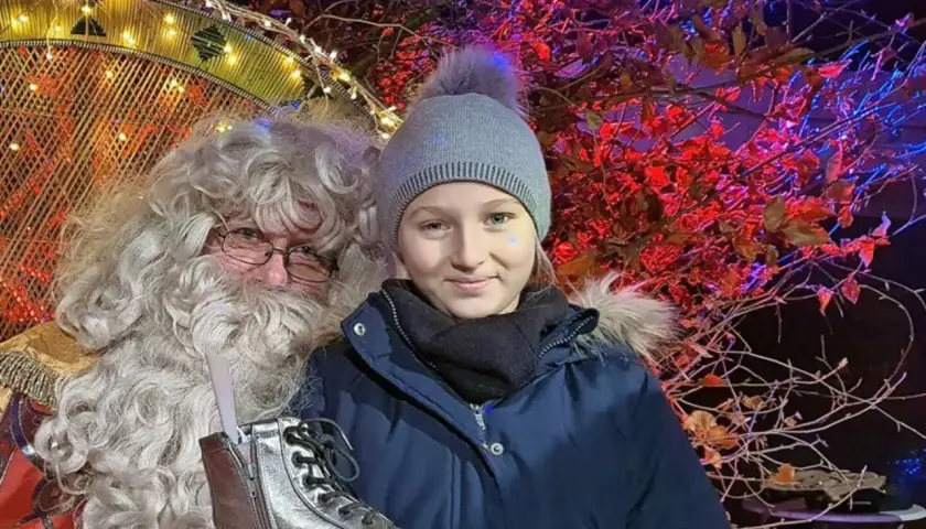 Ein Mädchen mit Mütze und Weihnachtsmann auf dem Weihnachtsmarkt Sassnitz. Er hält einen silbernen Stiefel.