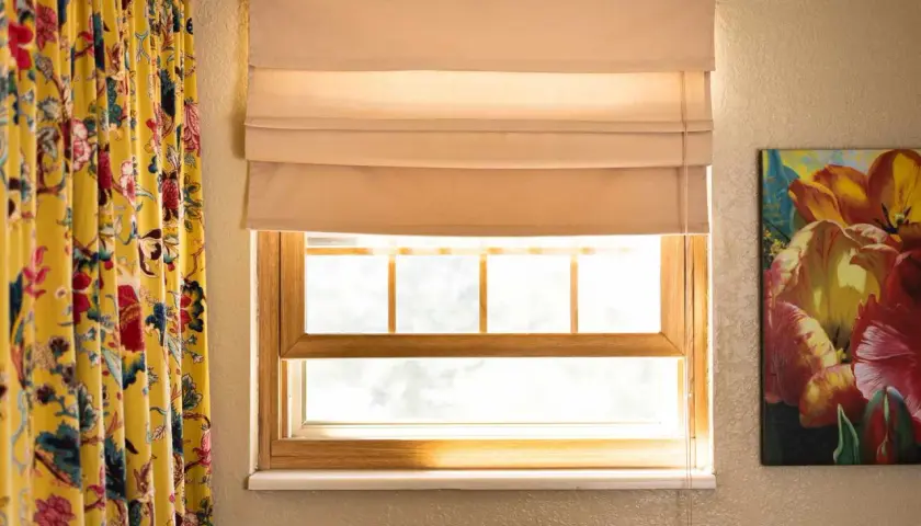 A beige Roman shade is partially lowered over a window, showing how to make Roman shades with its neat folds.