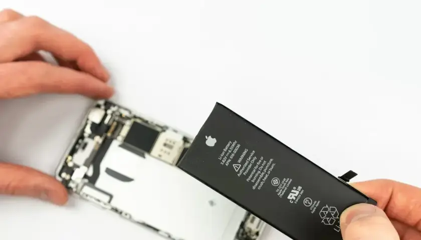 Wymiana iPhone przy niskiej kondycji baterii. Dłoń trzyma wyjętą baterię z telefonu.