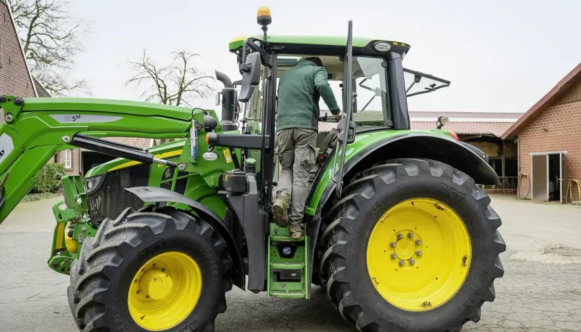 Rolnik wsiada do zielonego traktora John Deere, gotowy do pracy na gospodarstwie.