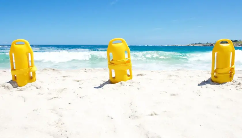 Trzy żółte bojki ratownicze na piaszczystej plaży. Zastanawiasz się, jaką bojka do pływania wybrać?