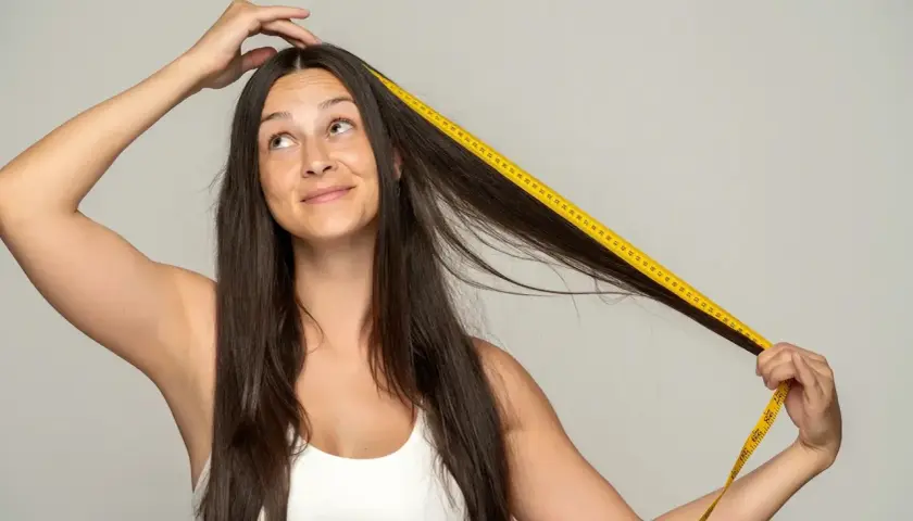 Mujer se mide el pelo con cinta métrica amarilla, preguntándose cuánto tarda el pelo en crecer.