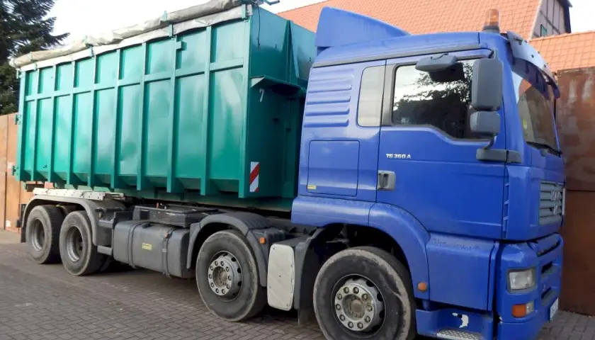 Blauer LKW mit großem grünen Container. Die Bedeutung eines solchen LKW ist der Transport von Schüttgut oder Abfall.