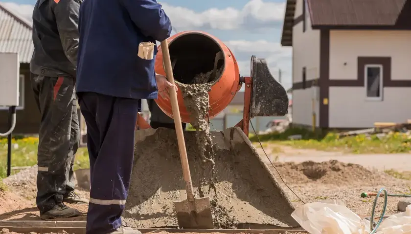 Dwóch budowlańców pracuje przy betoniarce. Wylewa się z niej świeży beton. Pytanie: ile cementu na betoniarkę 200?