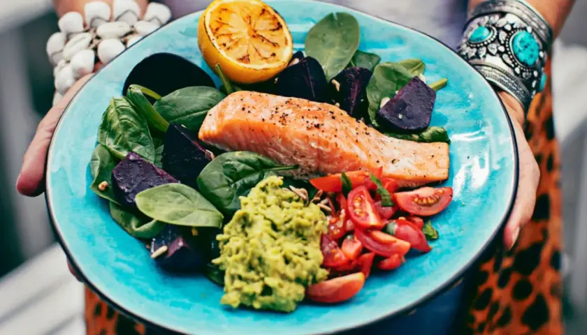 En matig sallad med lax, rödbetor, spenat, tomat, avokado och grillad citron på en turkos tallrik.