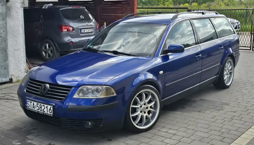 Błękitny Passat B5 1.9 TDI 130KM na aluminiowych felgach, zaparkowany na podjeździe obok szarego SUV-a.