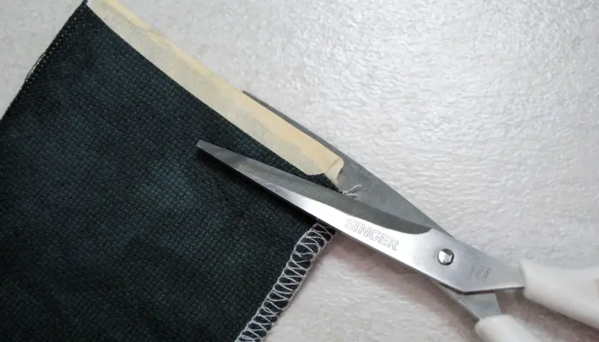 Singer scissors cut dark green corduroy fabric. The edge is serged, showing that corduroy does not fray easily.
