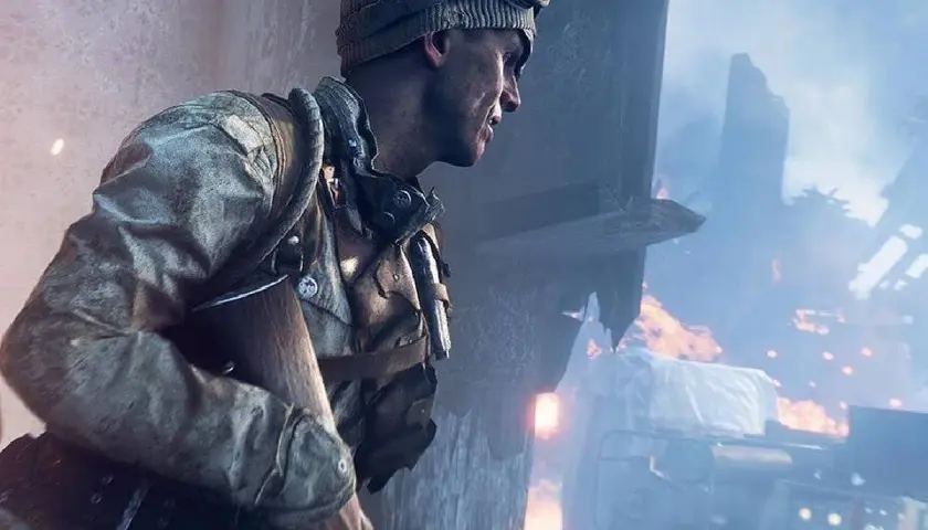 Żołnierz w czapce i goglach, gotowy do akcji w grze fps. W tle płonące ruiny i dym.