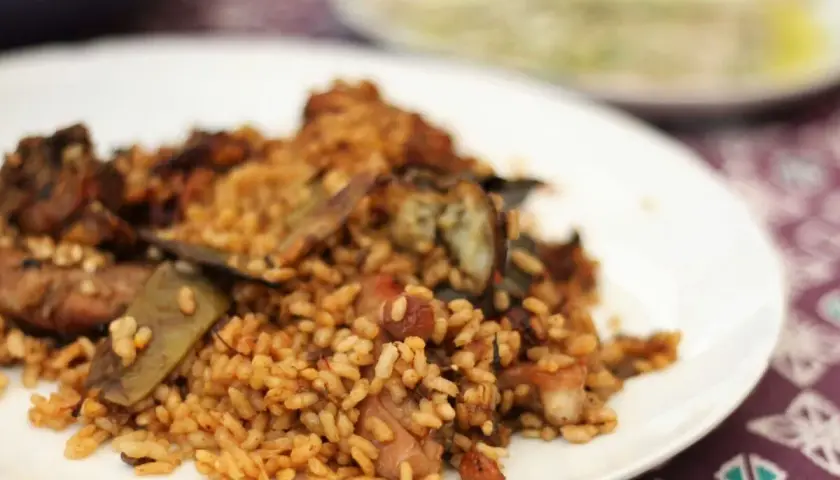 Deliciosa paella de conejo con trozos de carne dorada y verduras, servida en un plato blanco.