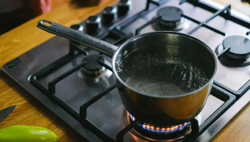 En kastrull med koksalt vatten bubblar på spisen. En grön paprika ligger bredvid.