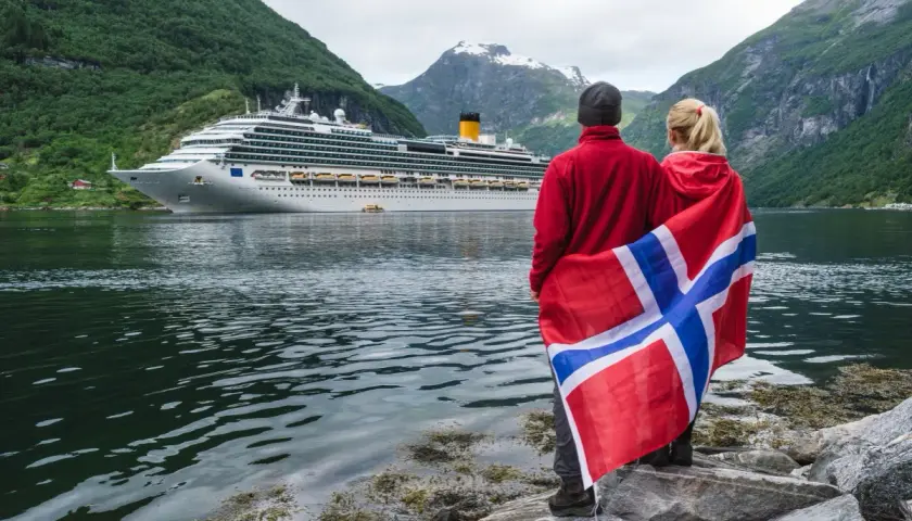 Para podróżuje po Norwegii, z flagą narodową i statkiem wycieczkowym w tle. Planujesz podróż? Pomyśl o ubezpieczenie Norwegia.