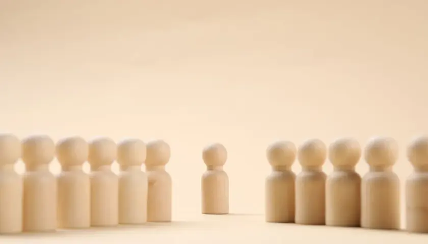 Un pupazzetto di legno si erge da solo, separato da un gruppo. Un simbolo di imparare a stare da soli, trovando forza nella propria individualità.