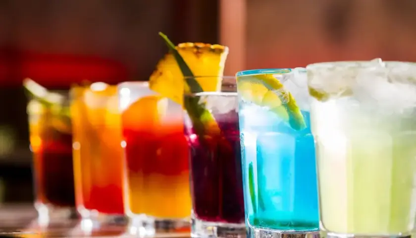 Rząd kolorowych, klasycznych drinków z lodem i owocowymi dekoracjami, gotowych do podania.