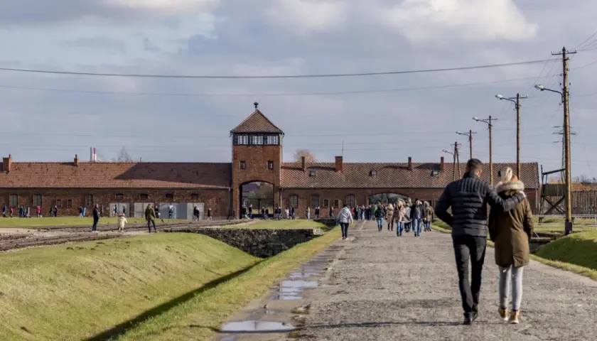Spacerując po terenie byłego obozu, zastanawiamy się, ile trwa zwiedzanie Auschwitz. Widać ludzi wchodzących przez bramę.