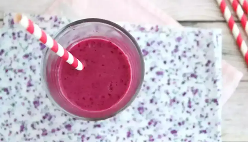 En glas med en lila indisk yoghurtdryck, med ett rött och vitt randigt sugrör.