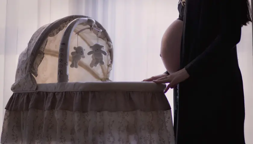 Gravid kvinna med händerna på en vagga med nallar, en fixerad bebis väntar.